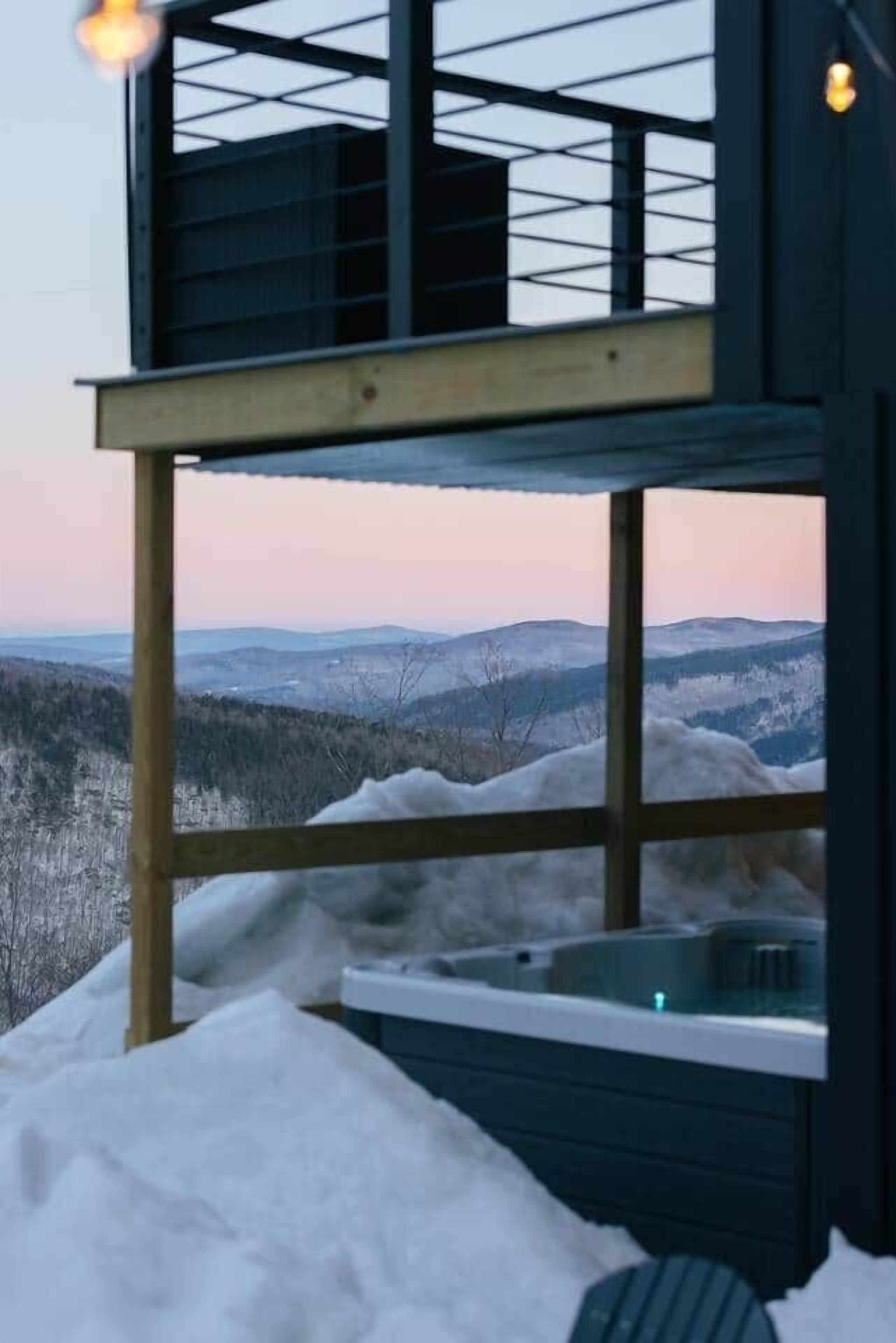 A two-story building with a hot tub on the ground floor and a view of a snowy landscape.