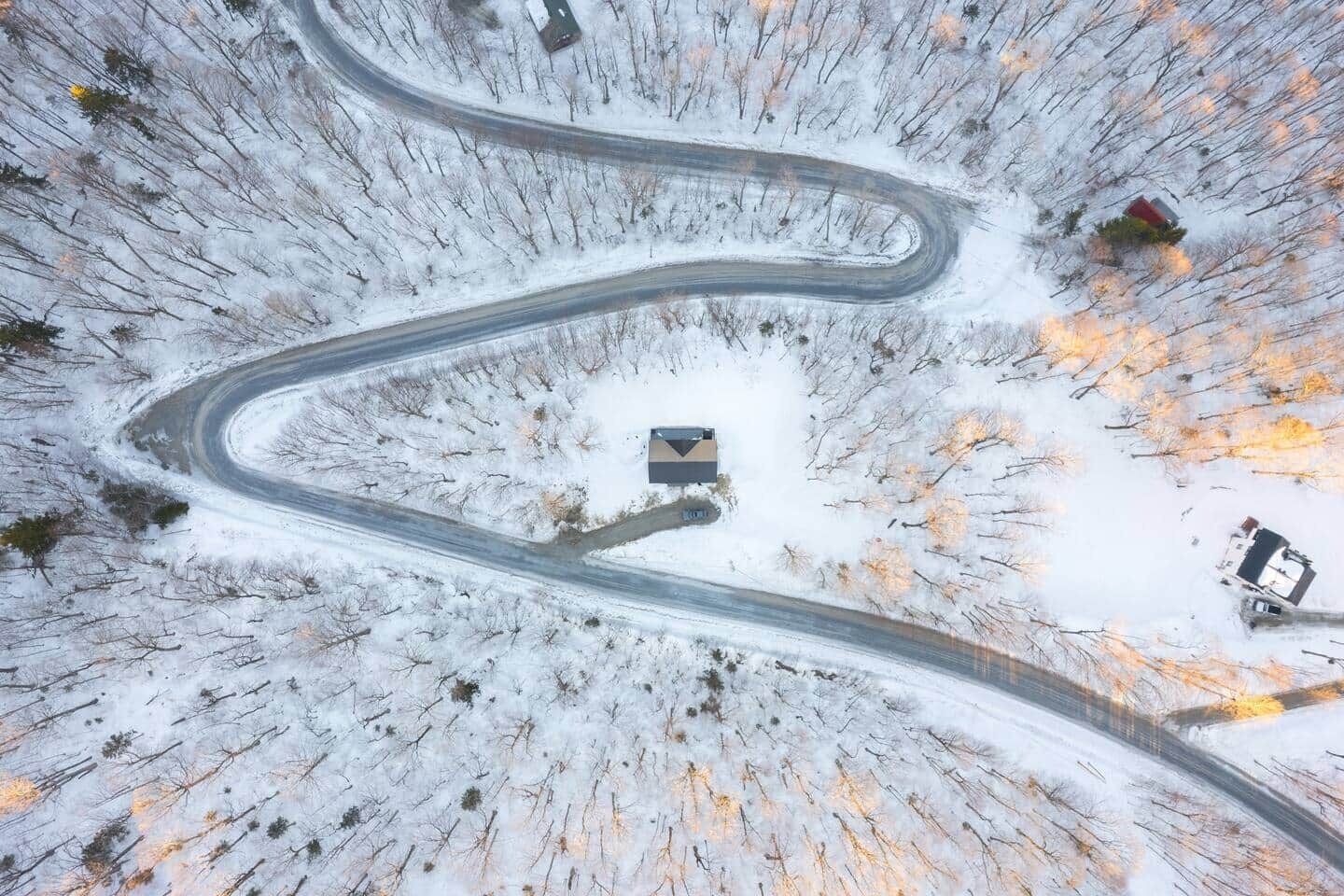 A winding road through a snowy landscape with a small building at the center.