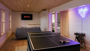 Ett rum med ett bordtennisbord, en soffa, en neonreklamskylt och en tv-skärm som visar ”NETFLIX”.