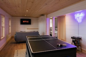 Una habitación con mesa de ping pong, sofá, un letrero de neón y un televisor que muestra 'NETFLIX'.