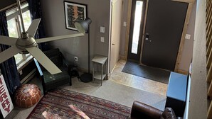 Een kamer met hoge plafonds, een plafondventilator, een leren bank in bruin, een kamerbreed tapijt en een groot raam met uitzicht op bomen.