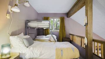 Een kamer met stapelbedden, een nachtkastje met lamp, een raam met gordijnen en uitzicht op bomen.