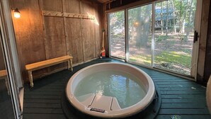 Een houten interieur met een bubbelbad, een bank en een groot raam.