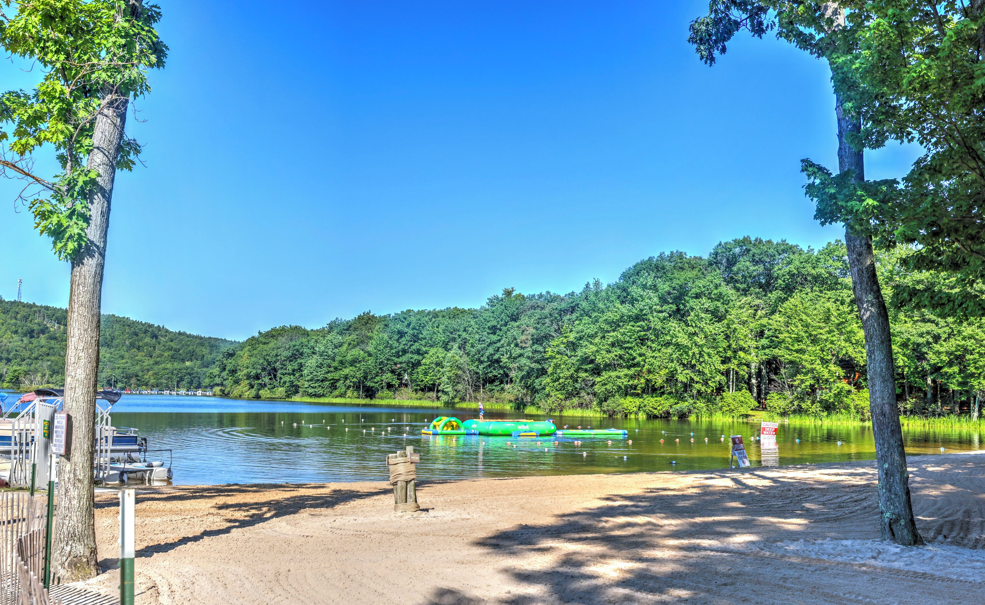 Un parco sul lago con una spiaggia sabbiosa, una zattera gonfiabile verde e un pontile con barche.