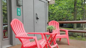 Een houten terras met twee rode Adirondack stoelen en een kleine tafel met een potplant. Een bord met de tekst 'The Porch Sit & Relax' is boven de deur te zien.