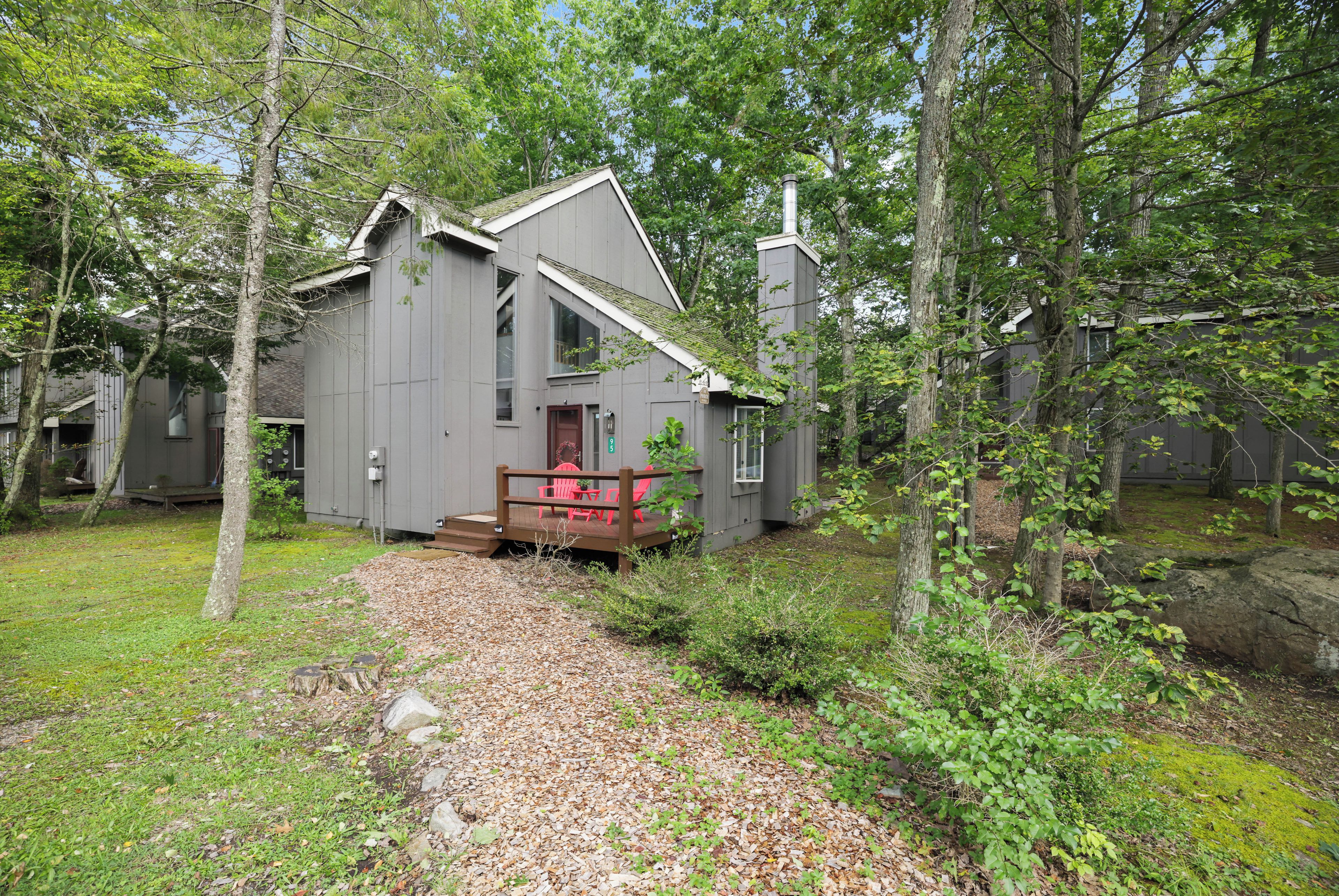 A cabin with a deck and outdoor seating, surrounded by trees.