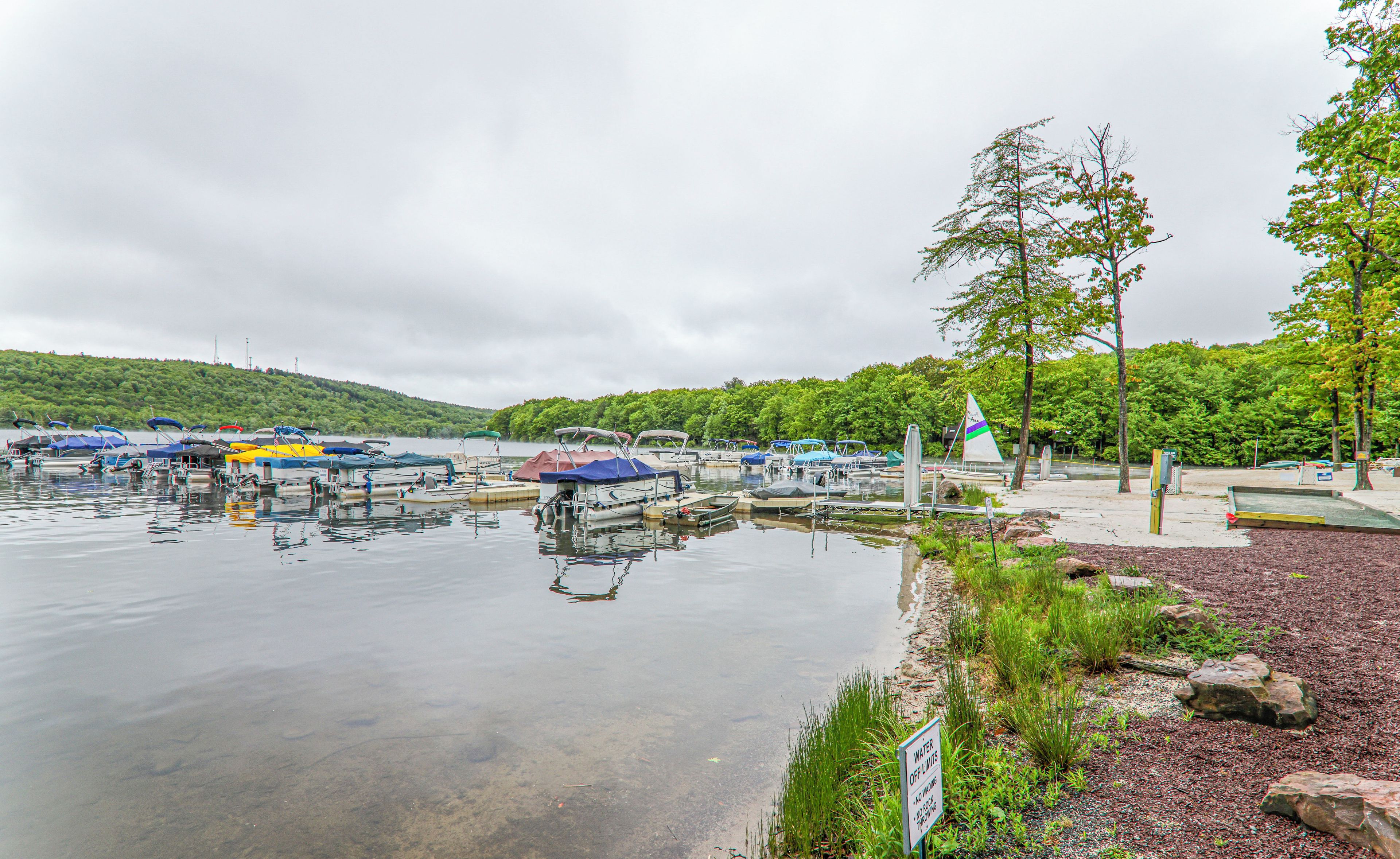 A marina with boats docked, a water off limits sign, and a hilly landscape in the background.