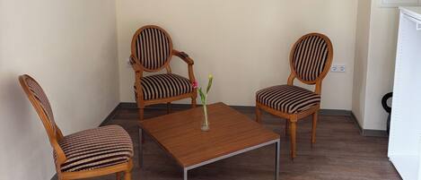 A room with two wooden chairs with striped upholstery, a square wooden table, and two framed pictures on the wall.