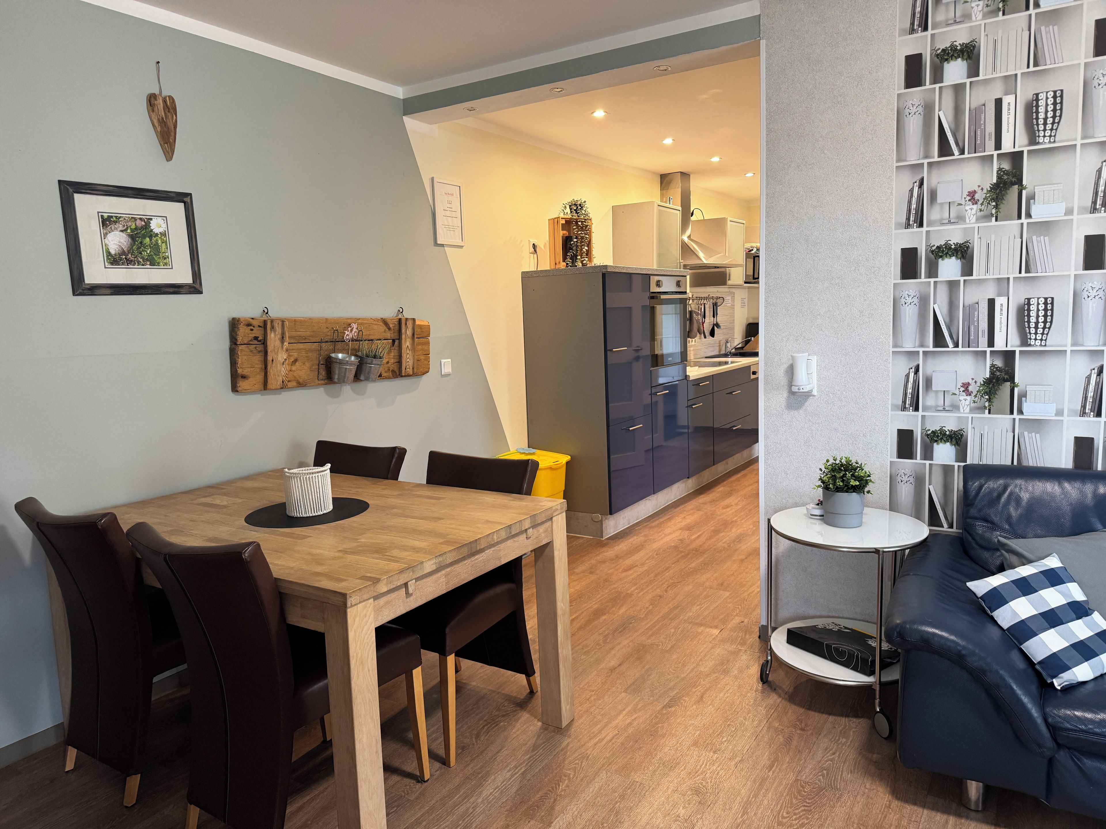 A modern living room with a dining table, dark leather sofa, and a bookshelf.