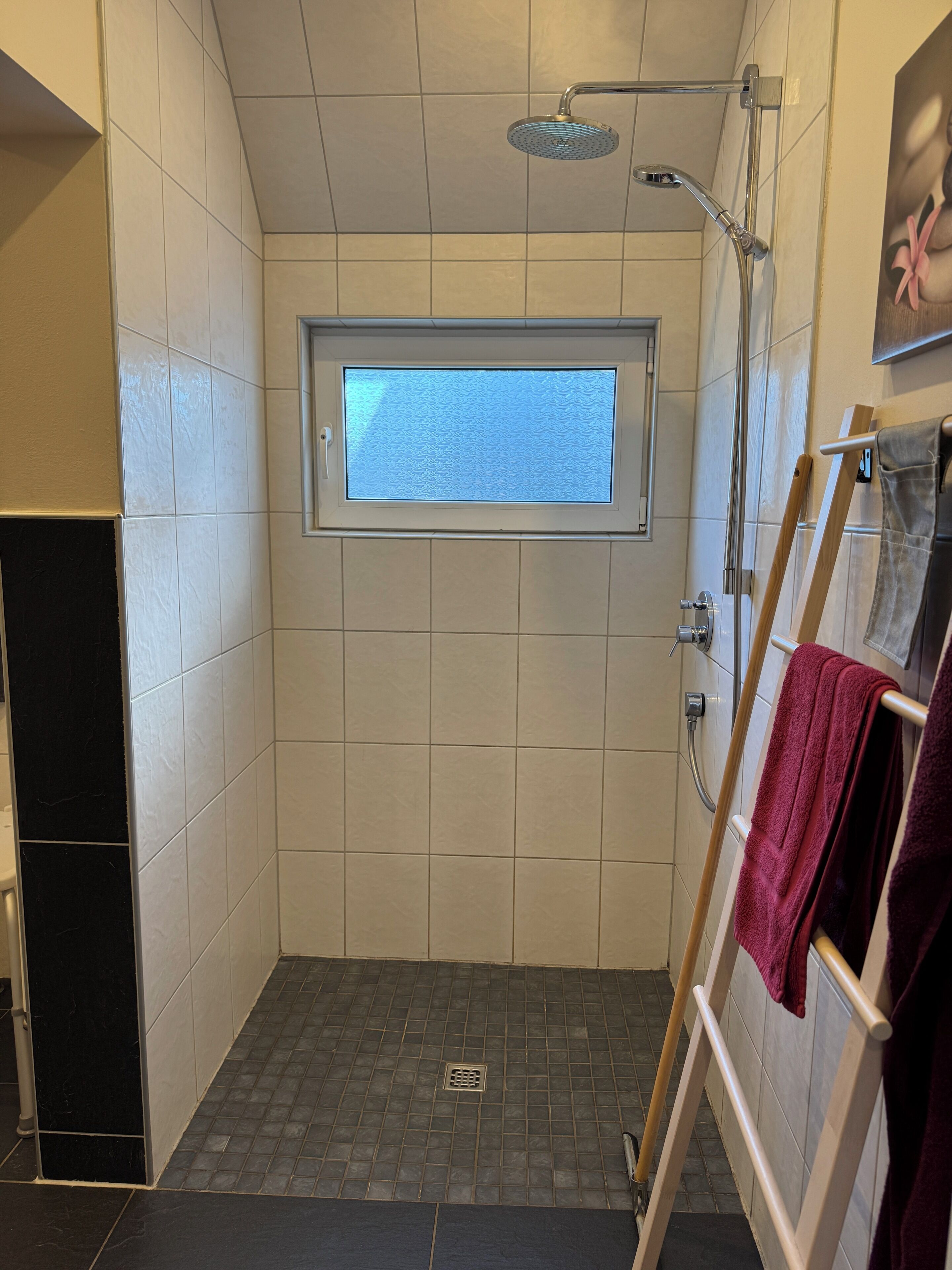 Eine Dusche mit Fenster, einem Handtuchhalter und einem Lüftungsgitter am Boden.