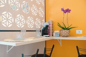 A dining area with a wooden partition, a coffee machine, a potted plant, and a set of glassware.