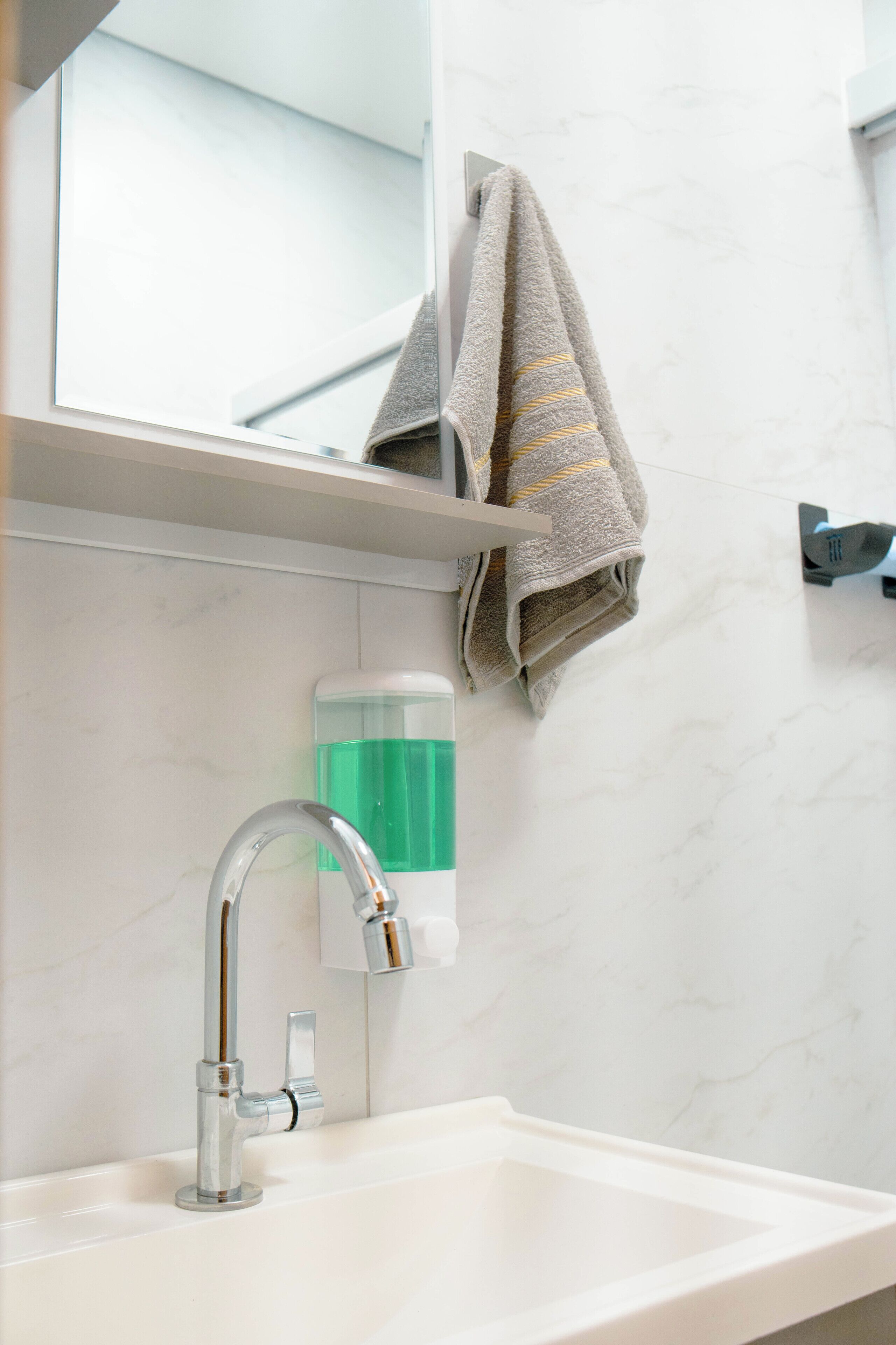 Une salle de bain avec un lavabo blanc, un miroir, un porte-serviettes avec une serviette et un distributeur de savon.