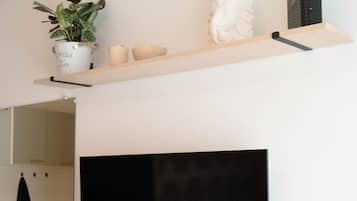 Uma cozinha moderna com uma televisão de tela plana na parede, uma prateleira de madeira acima com objetos decorativos e um vaso de planta.