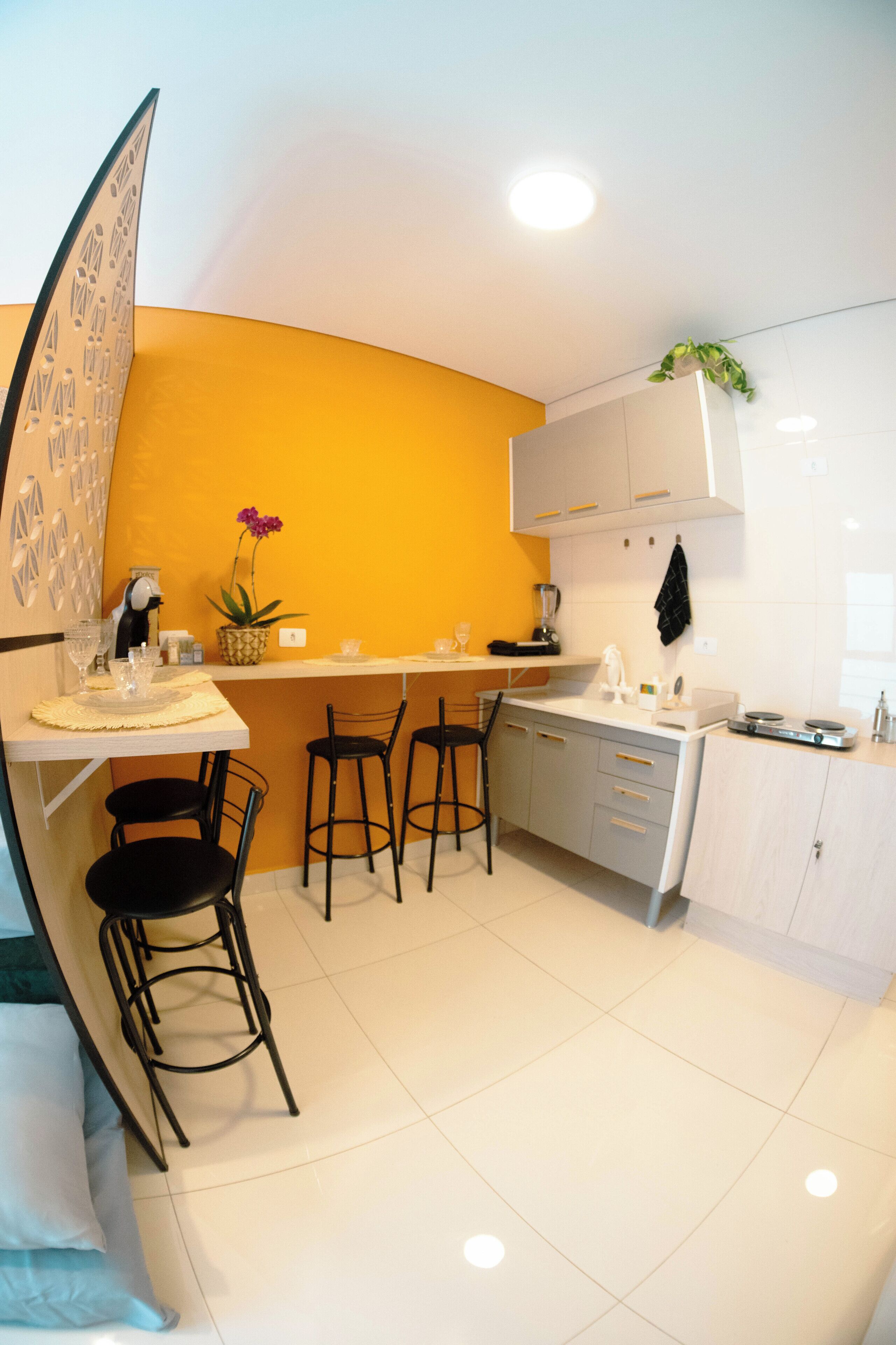 Une cuisine compacte avec un coin repas, comprenant un plan de travail blanc, des tabourets de bar et une petite plante en pot.