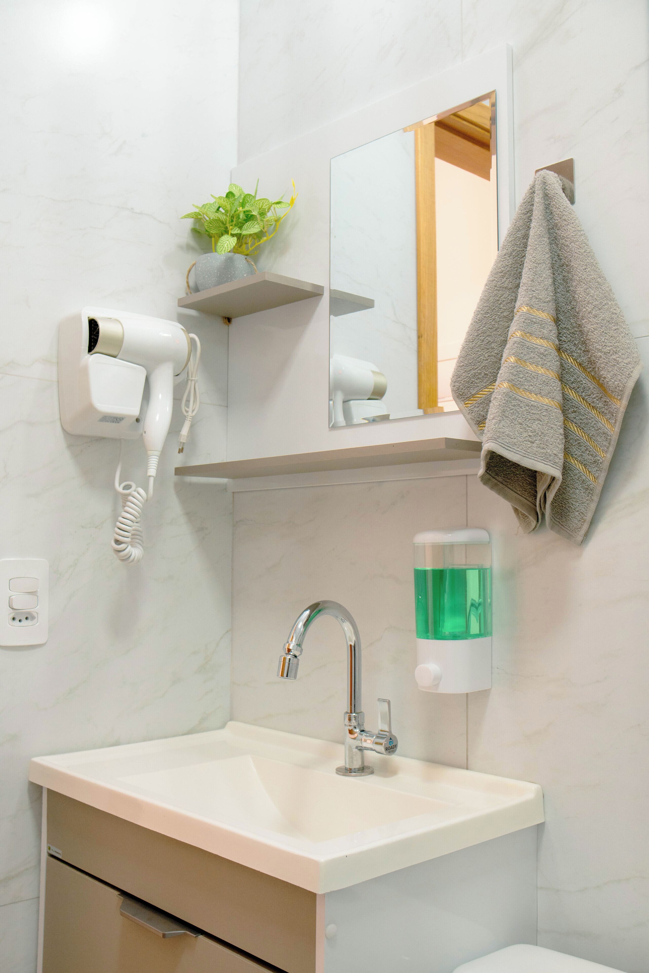 A bathroom with a sink, a mirror, a towel rack, a hairdryer, and a soap dispenser.