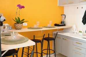 Cozinha com parede amarela, área de bar com banquetas, liquidificador e uma orquídea em vaso.