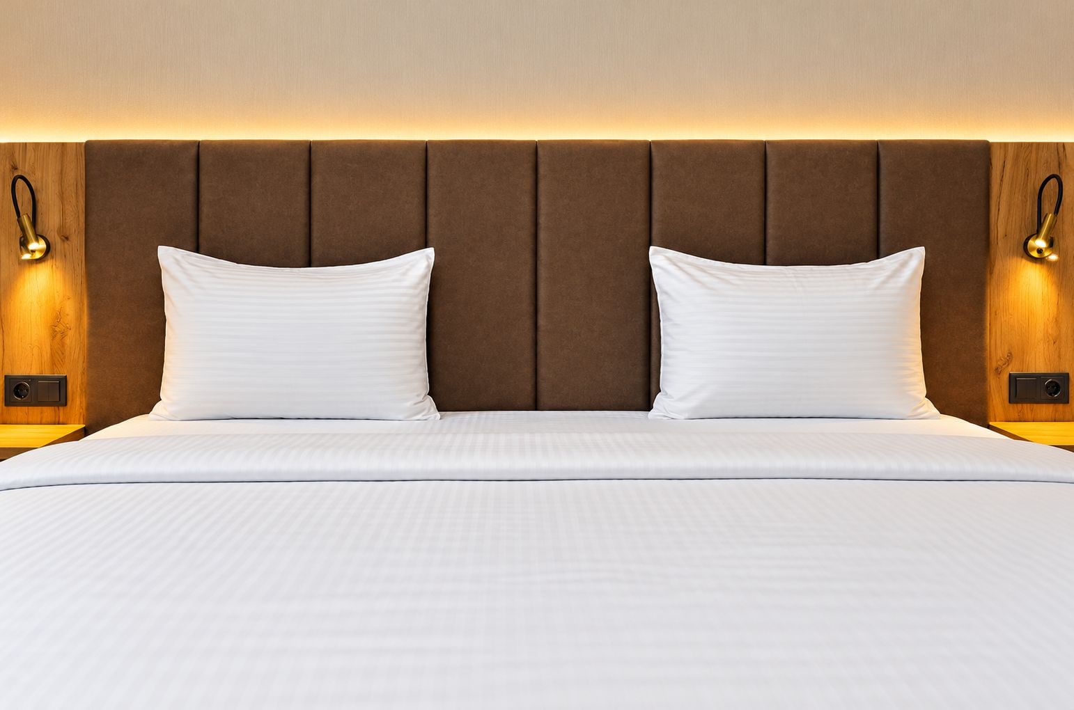 Habitación de hotel con una cama grande, dos almohadas, cabecero de madera y lámparas fijadas a la pared.