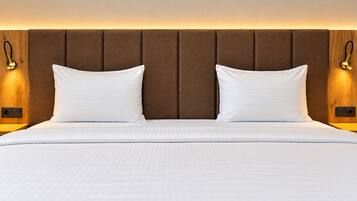 Habitación de hotel con una cama grande, dos almohadas, cabecero de madera y lámparas fijadas a la pared.