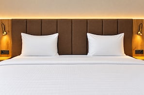 A hotel room with a large bed, two pillows, a wooden headboard, and wall-mounted lamps.