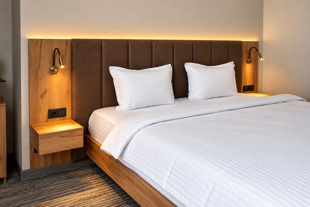 A hotel room with a large bed, two bedside tables, and wall-mounted lighting.