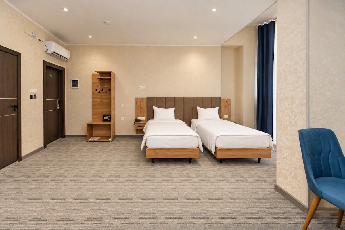 A hotel room with two single beds, a wooden headboard, a blue chair, and a built-in shelf.