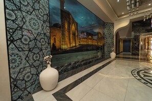 Un vestíbulo con un gran mural en la pared, un jarrón blanco y suelo de mármol.