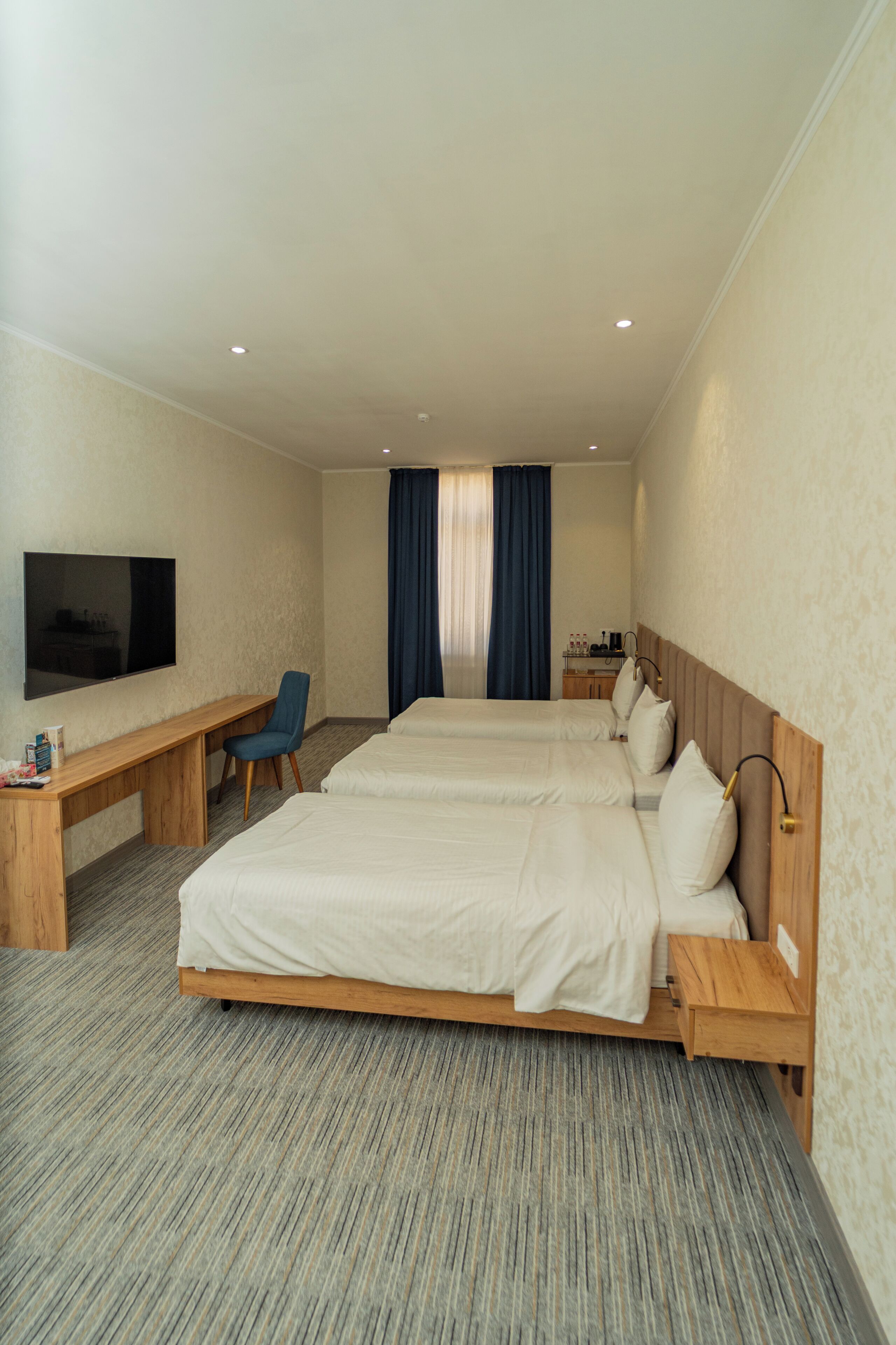 Habitació d'hotel amb dos llits, un escriptori, una cadira, un televisor i una finestra amb cortines.