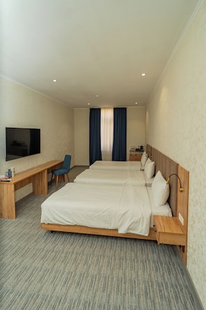 Habitación de hotel con dos camas, un escritorio, una silla, un televisor y una ventana con cortinas.