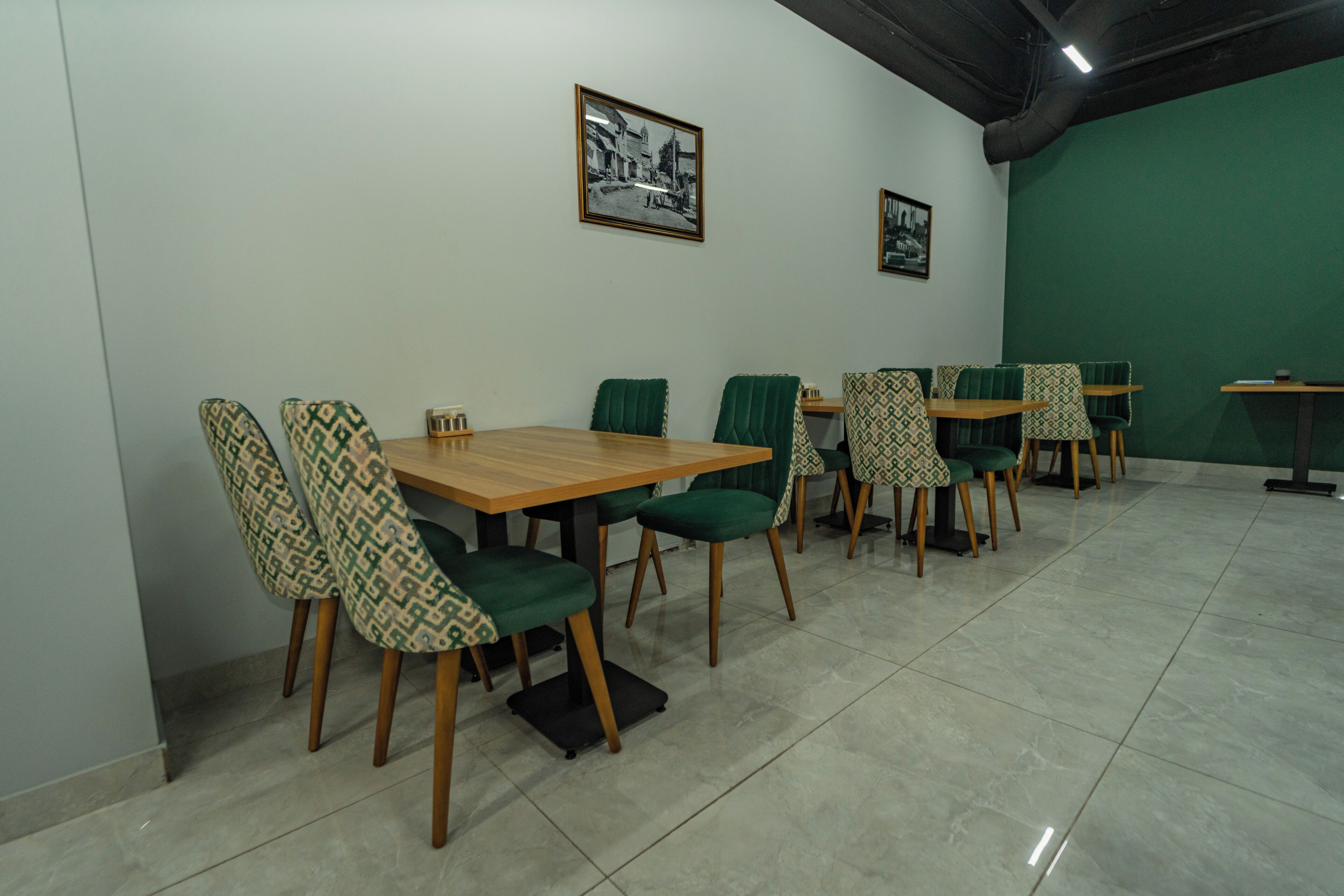 A dining area with tables and chairs, a green wall, and framed pictures on the wall.