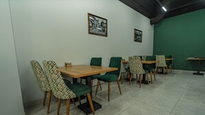 A dining area with tables and chairs, a green wall, and framed pictures on the wall. - Hanzade Palace  (Samarkand)