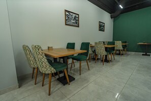 Un comedor con mesas y sillas, una pared verde y cuadros en la pared.
