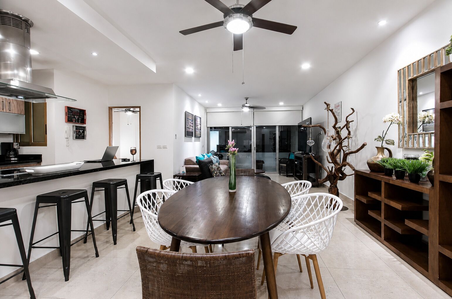 A modern kitchen with a central island, bar stools, a dining table with chairs, and a ceiling fan.