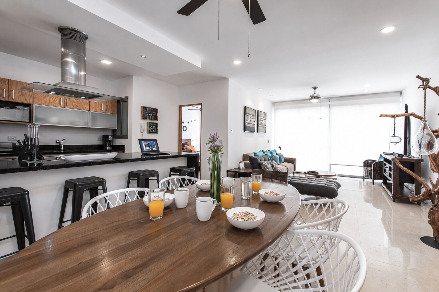 Una cocina moderna con zona de comedor, que incluye una mesa de madera, taburetes de bar y un espacio de estar con sofá y mesa de centro.