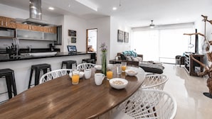 Eine moderne Küche mit Essbereich, ausgestattet mit einem Holztisch, Barhocker und einer Sitzecke inklusive Sofa und Couchtisch.