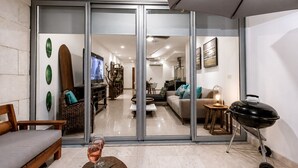 Ein modernes Wohnzimmer mit Glastür zum Essbereich, eine Couch, ein Couchtisch mit einem Weinglas und ein Grill.