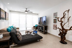 A modern living room with a sofa, a coffee table, a TV, and a decorative wooden sculpture. - Modern Apartment Pool & Balcony (Playa del Carmen)