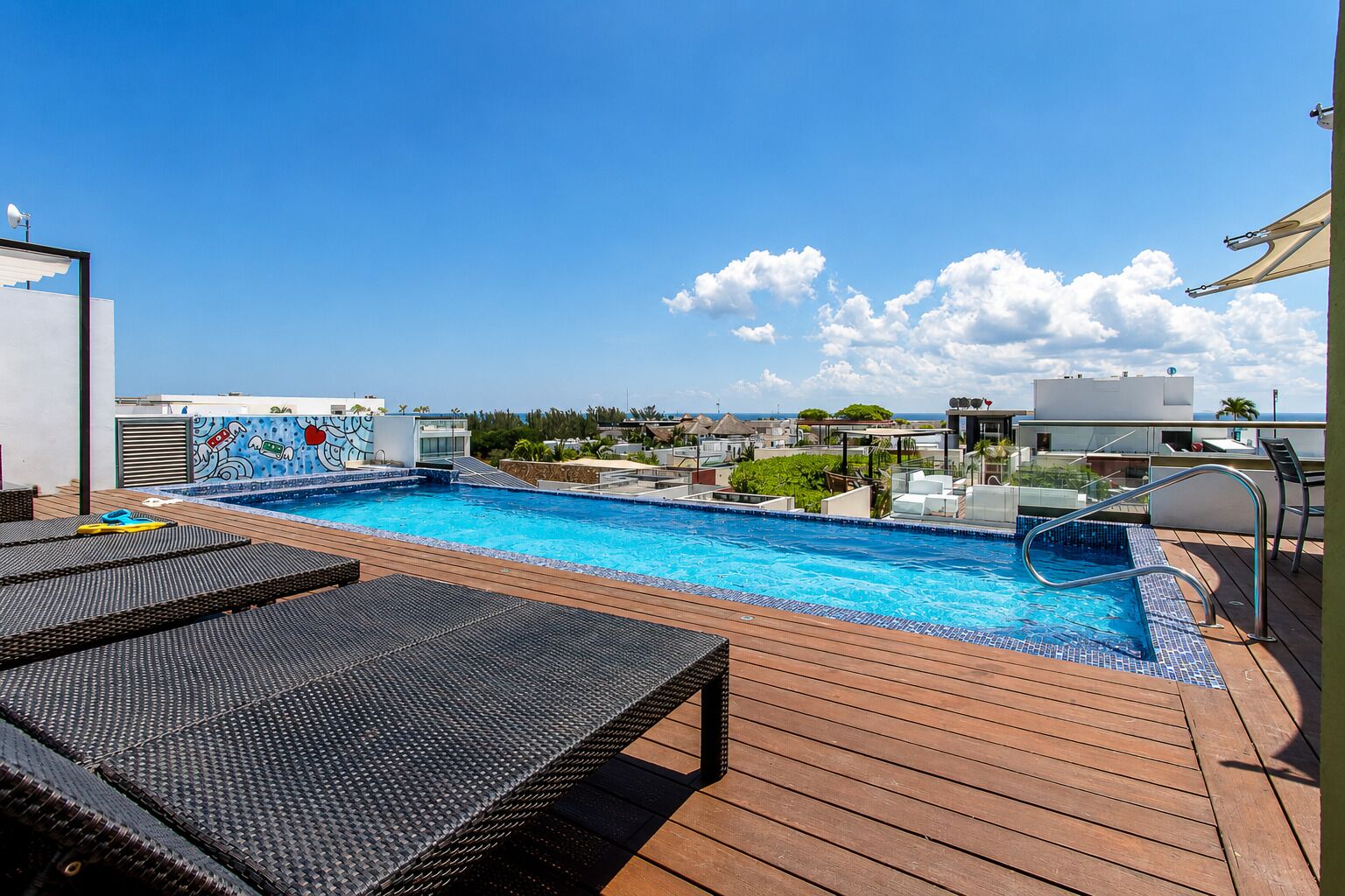 A rooftop pool area with lounge chairs, a swimming pool, and a view of the ocean.