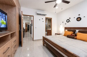A bedroom with a bed, a TV, a ceiling fan, and a bathroom visible through an open door. - Modern Apartment Pool & Balcony (Playa del Carmen)