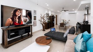 Ein modernes Wohnzimmer mit Flachbildfernseher, Couchtisch, Sofa, Essbereich mit Tisch und Stühlen sowie Küchenzeile mit Herd.
