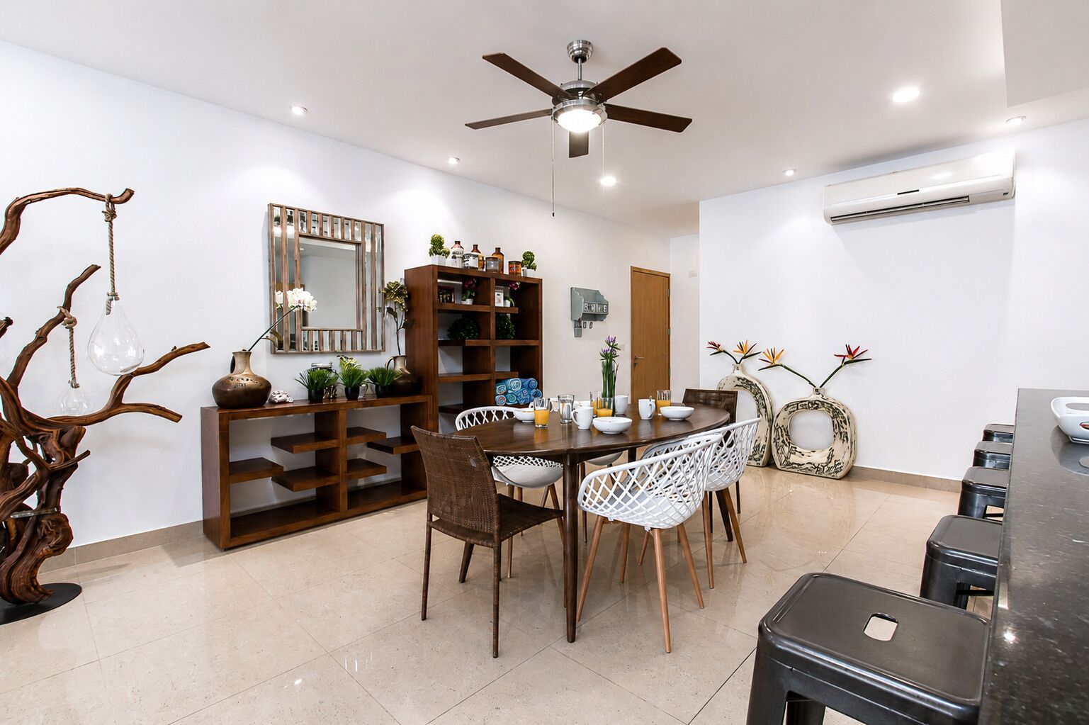A dining area with a round table, white chairs, a ceiling fan, and a wooden bookshelf.