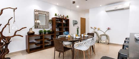 Un comedor con una mesa redonda, sillas blancas, un ventilador de techo y una estantería de madera.