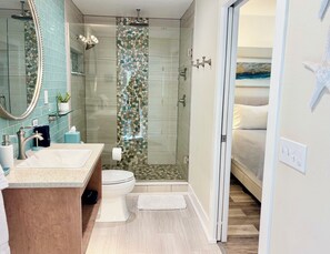 Une salle de bain avec une douche en verre, un lavabo avec un miroir et des toilettes.
