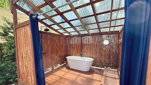 Eine Holzterrasse mit freistehender Badewanne, einer Bank und einem Bambuszaun.