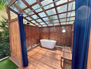 Eine Holzterrasse mit freistehender Badewanne, einer Bank und einem Bambuszaun.