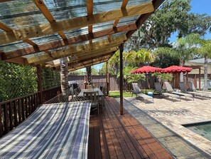 Une terrasse extérieure couverte avec une piscine, des meubles en bois et des parasols rouges.