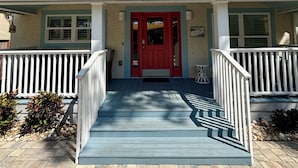 Ein zweistöckiges Haus mit roter Tür, einer Veranda mit weißen Geländern und einem blauen Dach.