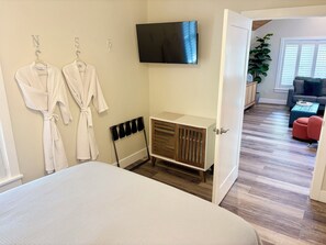 A hotel room with a bed, a TV mounted on the wall, a wooden cabinet, and a view of the living area. - Gorgeous Hideaway w/pool in Historic Downtown NSB (New Smyrna Beach)