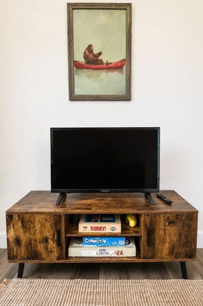 Uma estante de madeira com um televisor de tela plana, um quadro emoldurado acima e jogos de tabuleiro embaixo.