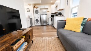 A compact living space with a television, a sofa, a coffee table, a kitchen area with appliances, and a laundry machine.