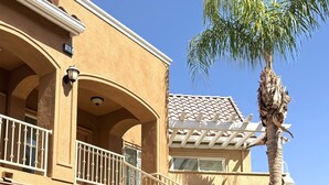 Un edificio de varios pisos con balcón, una palmera y una escalera.